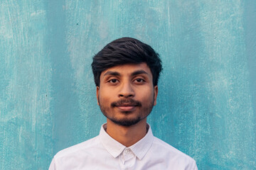 A brown boy portrait looking at the camera wearing white shirt with little beard