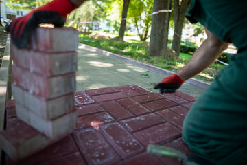 A construction worker kneels to lay paving stones on a sunny day.