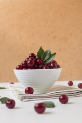 Cherry berries in a white cup on the table on a light background, modern rustic style