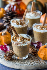 Four pumpkin spice chia puddings on a rustic board with autumn decorations.