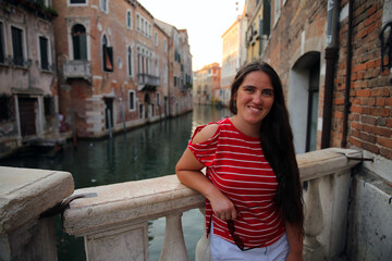 Fototapeta na wymiar A girl in a red shirt with white lines posing in front of a canal in Venice, Italy