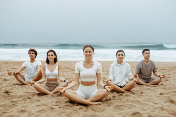 Youngsters finding balance with beach yoga, meditating in lotus position, enjoying morning training on ocean shore