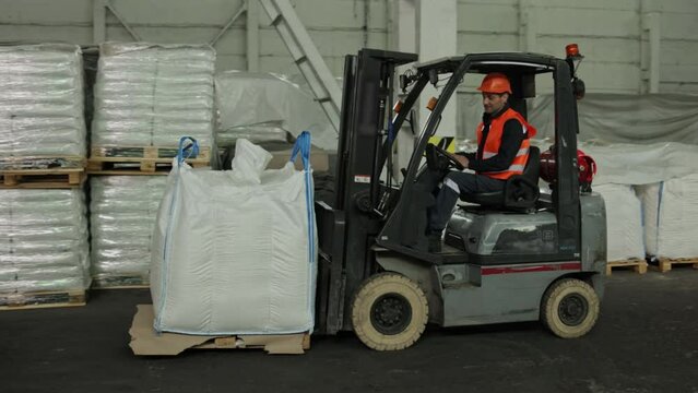 Warehouse organization, Stock arrangement, Operator skills. Warehouse employee is working alongside forklift loader to navigate pallets.