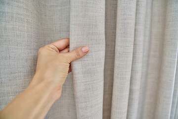 Light beige sand linen natural curtains on window, close-up of hand touching curtains
