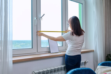 Woman measuring window with tape measure, tailoring service
