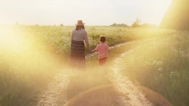 A mother walks hand in hand with her son while walking along a country road. Happy together parental love happiness and freedom concept. High quality 4k footage