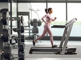 Fototapeta premium Full profile shot of a female running on a treadmill at a gym