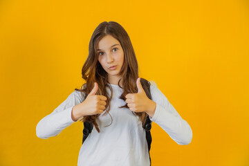 little cute schoolgirl with backpack over her shoulders keeps her fingers up in gesture up