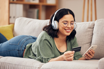 Woman, credit card and phone on sofa, home and headphones with smile, online shopping or payment on...