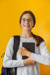 Vertical portrait little joyful cute girl in glasses with backpack holding notepad in her hands