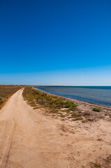Fototapeta na wymiar Dirt road along the salt lake against a clear blue sky