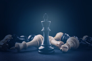 Black king among fallen chess pieces on black background, dark blue toned
