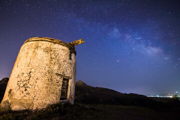 Ruin windmill in the night sky. A view of the stars of the Milky Way with a mountain top in the...