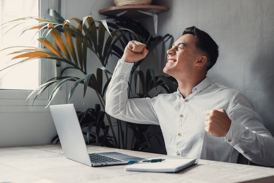 Man sit at desk read e-mail on laptop makes yes gesture feels happy. Male entrepreneur get great business news, celebrate career growth, advance. Achievement, win, moment of auction victory concept.