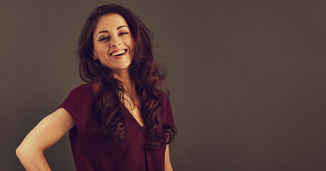 Beautiful natural makeup toothy smiling woman with long brown curly healthy hair style looking happy. Closeup portrait on studio background with empty copy space. Toned