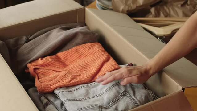 Donation clothes or preparing for move. Person packing apparel into cardboard box.
