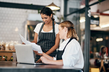 A connected team keeps the numbers up. Shot of two women using a laptop together while working in a cafe.