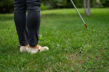 Close-up of the legs of an elderly woman using a tactile cane on a walk in the park. 