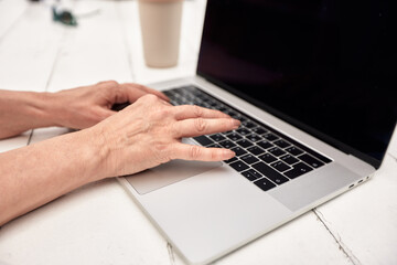 Close up of mature woman's hands working with laptop at the table of outside cafe. Middle-aged lady works and plays using modern technology. Active lifestyle for elderly.