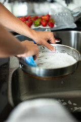 close up of a young adult male washing dishes at the kitchen sink with in a light and airy kitchen