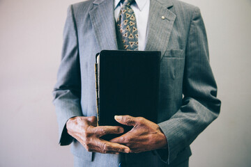 close up cropped photo of a man holding his bible wearing a suit and tie in church pastor african american black man - Powered by Adobe