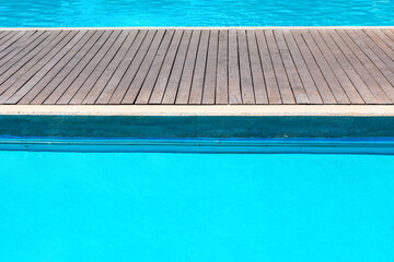 Swimming pool with wooden decking and blue water in the background