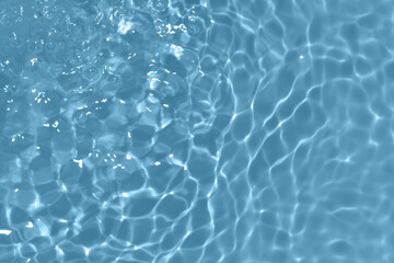 Blue water with ripples on the surface. Defocus blurred transparent blue colored clear calm water surface texture with splashes and bubbles. Water waves with shining pattern texture background.