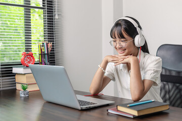 Smiling asian teen girl with glasses and wearing headphones having fun looking at laptop computer.