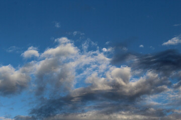 Cielo azul con nubes blancas y grises y luna llena entre las nubes. 