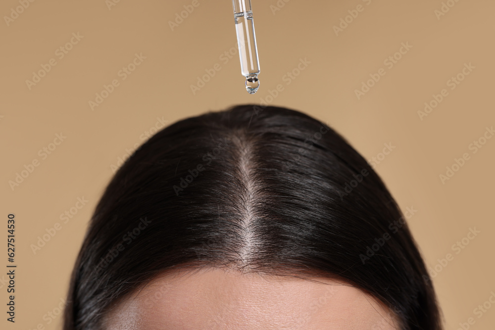 Wall mural Woman applying essential oil onto hair roots on beige background, closeup