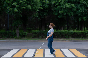 Blind pregnant woman crosses the road at a crosswalk with a cane. 