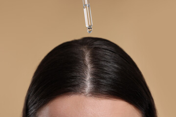 Woman applying essential oil onto hair roots on beige background, closeup