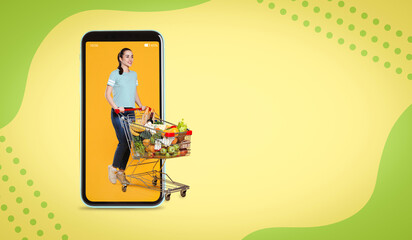 Happy woman with shopping cart full of groceries walking out huge smartphone on color background. Design with space for text