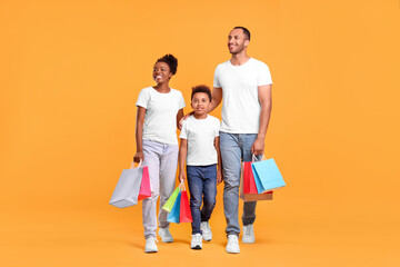 Family shopping. Happy parents and son with colorful bags on orange background