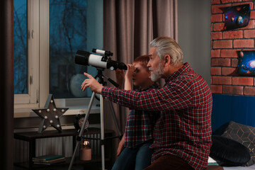 Little boy with his grandfather looking at stars through telescope in room
