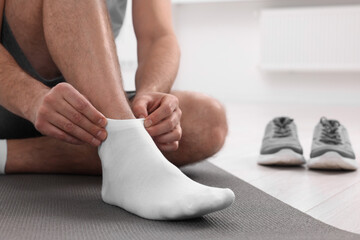 Man putting on white socks indoors, closeup. Space for text