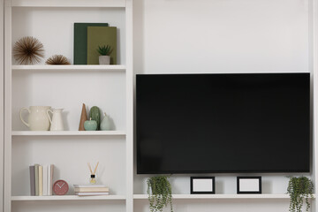 TV set and stylish shelves with decorative elements and houseplants near white wall. Interior design