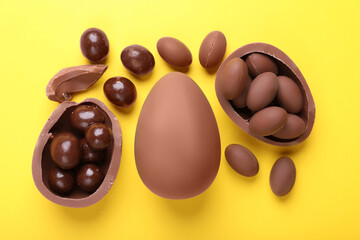 Delicious chocolate eggs and sweets on yellow background, flat lay