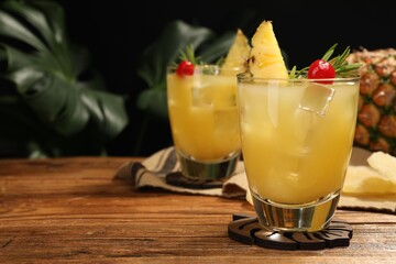 Glasses of tasty pineapple cocktail with rosemary and cherry on wooden table. Space for text