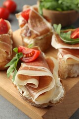 Tasty sandwiches with cured ham, tomatoes and arugula on wooden board, closeup