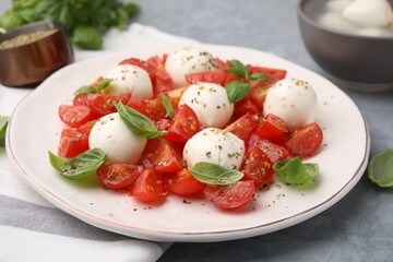 Tasty salad Caprese with tomatoes, mozzarella balls and basil on grey table, closeup