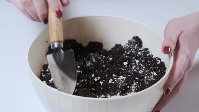 The girl mixes the soil and perlite with a small shovel for transplanting indoor flowers