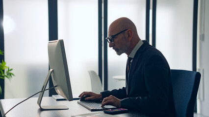 Middle-aged white man in a suit working in the office with desktop PC.