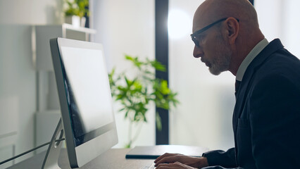 Middle-aged white man in a suit working in the office with desktop PC.