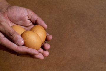 a man's hands holding three eggs together giving the feeling of showing them off or handing them over,defocused brown wooden background and with space for text