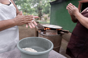 Two adult Hispanic women are shaping corn tortillas by hand