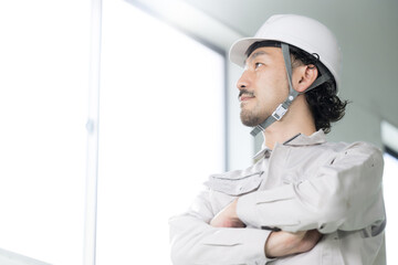 腕を組んで見上げる作業着の男性　未来や目標希望を見つめる横顔