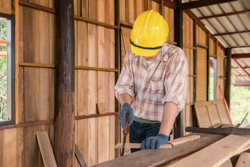 Asian carpenter cutting wood with hand saw on construction site build a house in the countryside