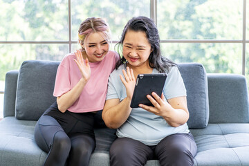 Happy senior asian mother and young daughter waving hands looking at web camera using tablet for video call, smiling mom and girl having fun greeting online by computer webcam making videocall