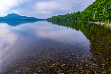 曇り空の下の静水の湖と湖畔の森の緑の木々。日本の北海道の屈斜路湖。